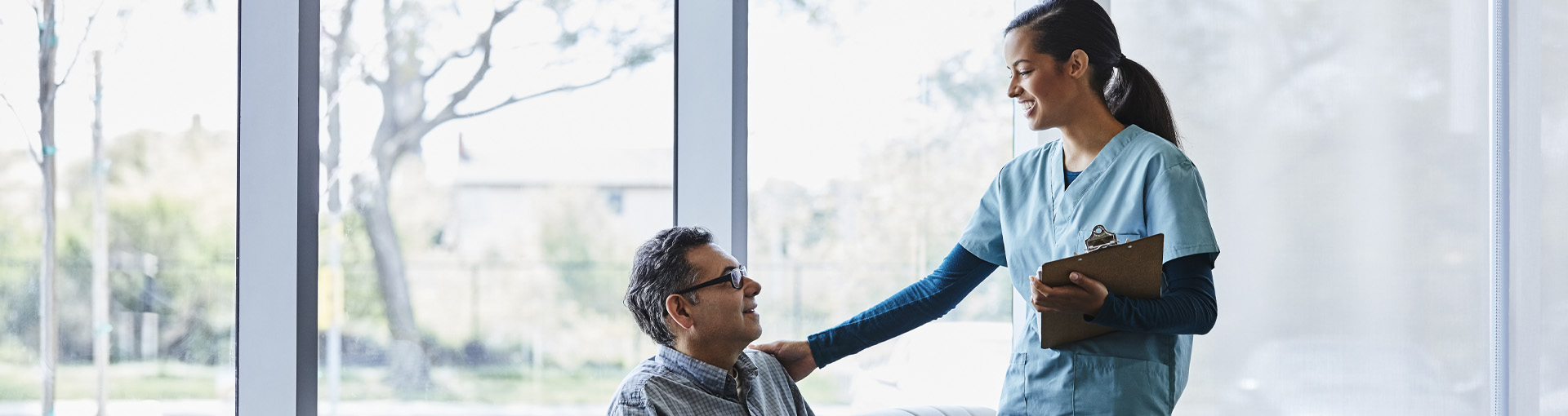 Een zorgprofessional van DNV biedt zorg en ondersteuning aan een zittende patiënt in een lichte, moderne faciliteit.