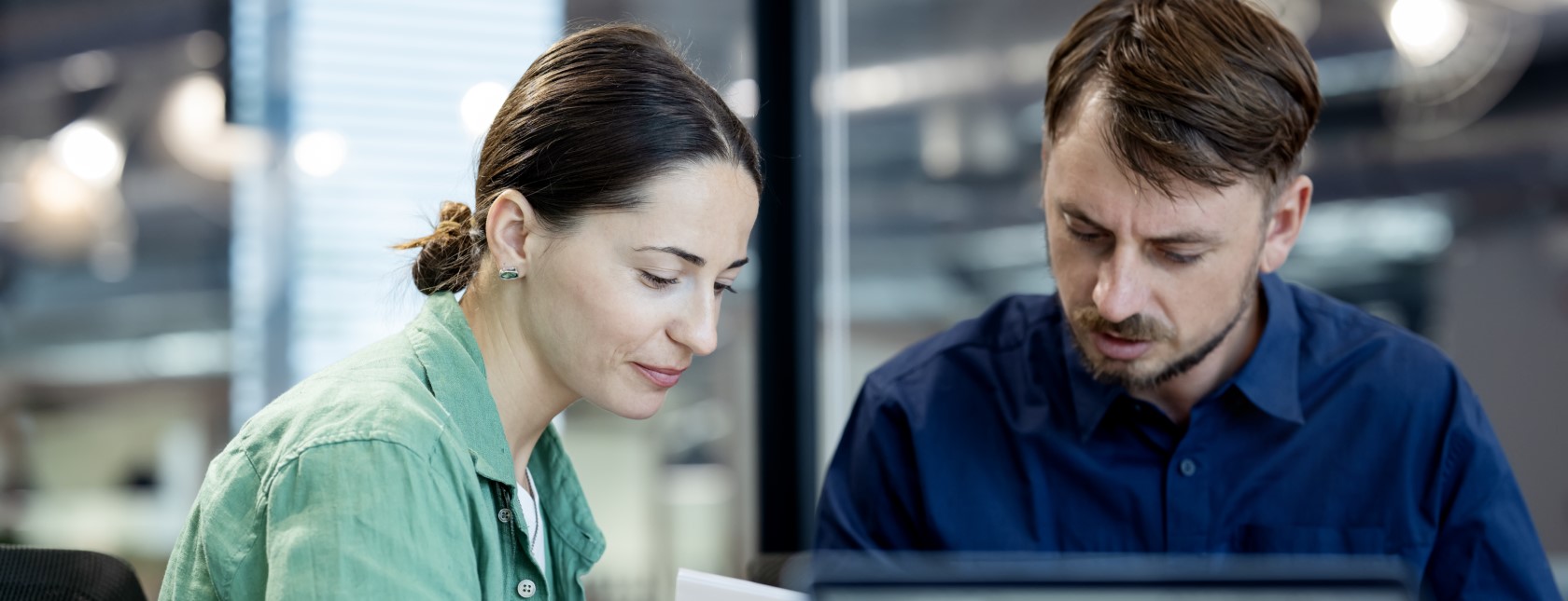 Een man en een vrouw die op kantoor aan het werk zijn en naar de tafel kijken.