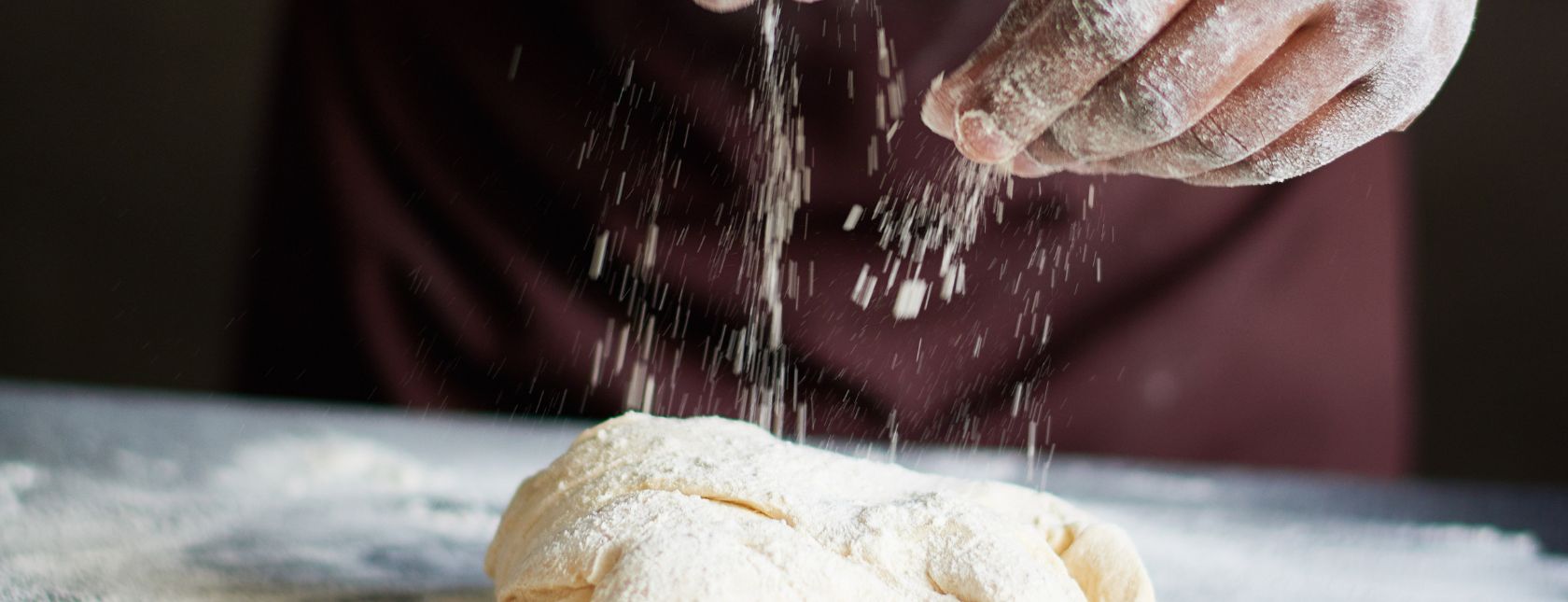 Bakker besprenkelt deeg met bloem