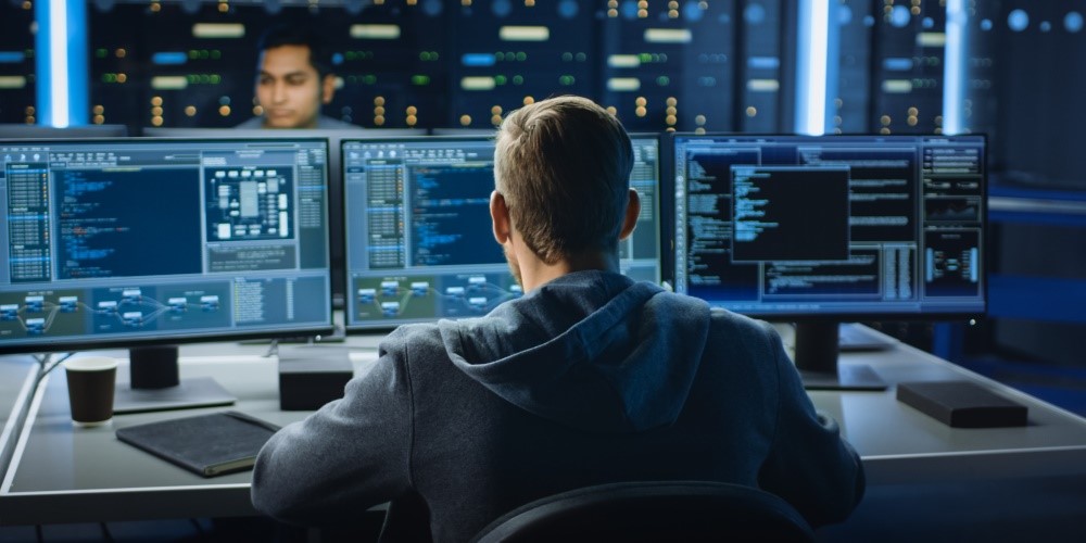 Een man die voor drie computermonitors zit te werken.